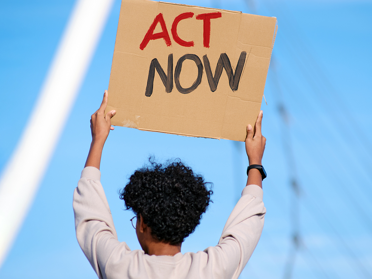 Rear view of a young woman raising arms and holding a placard with the words "ACT NOW"