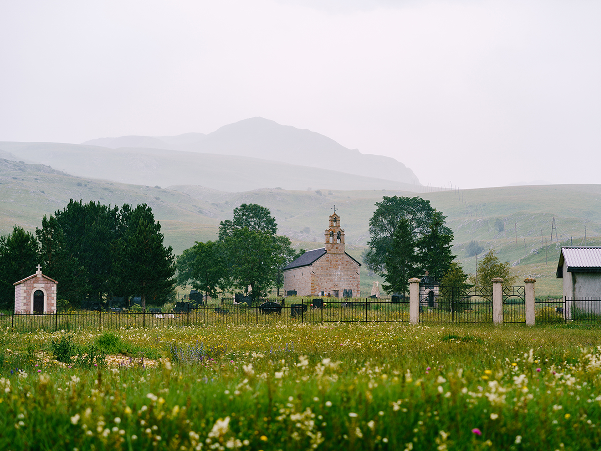 Small old brick church on a green meadow at the foot of the mountains