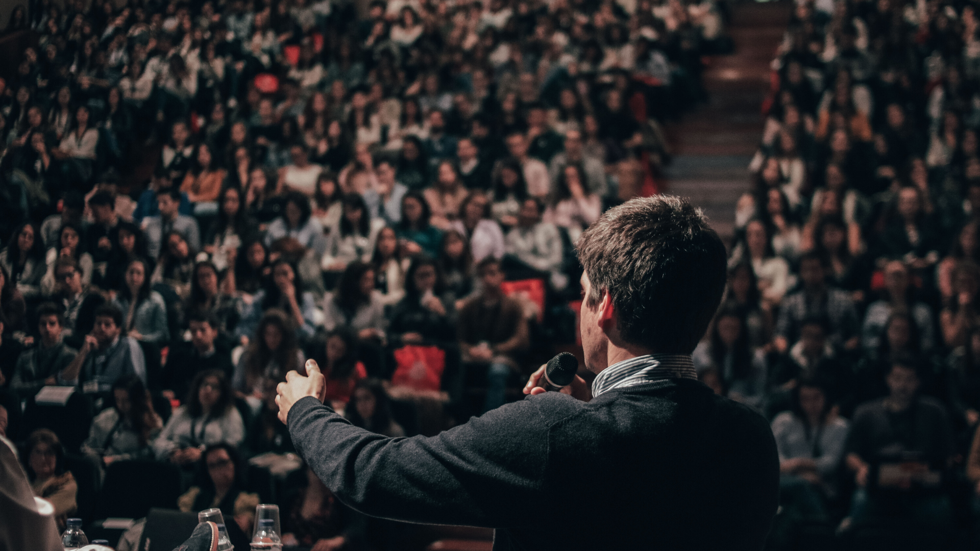 the back of a man speaking to a large auditorium filled with people