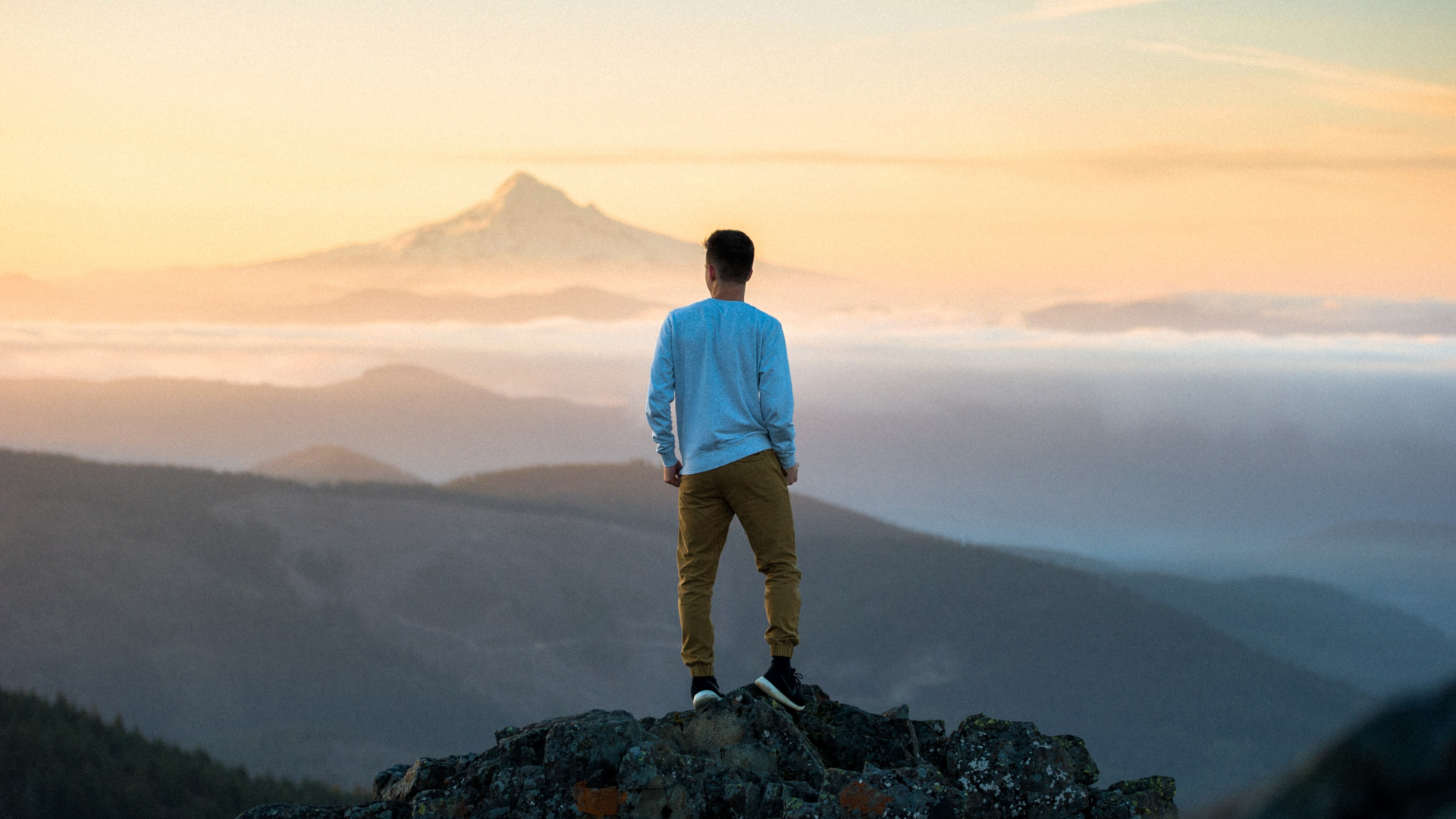 a man on a mountain peak gazes at a beautiful view of mountains during sunset hour