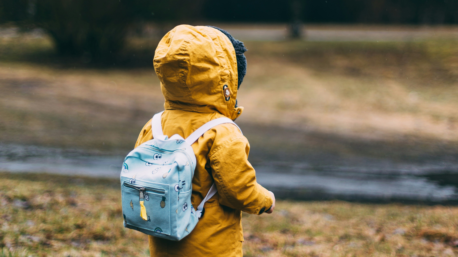the back of a young kid wearing a yellow raincoat and wearing a backpack on a rainy day