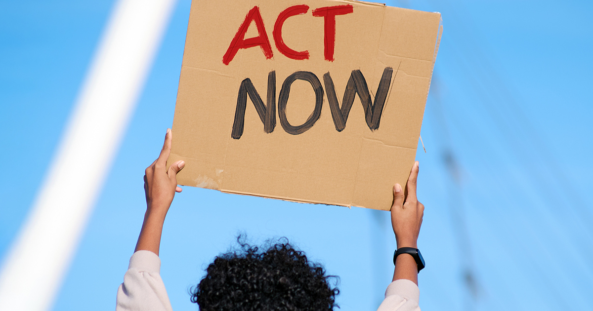 a person holding up a cardboard sign that says "Act Now"
