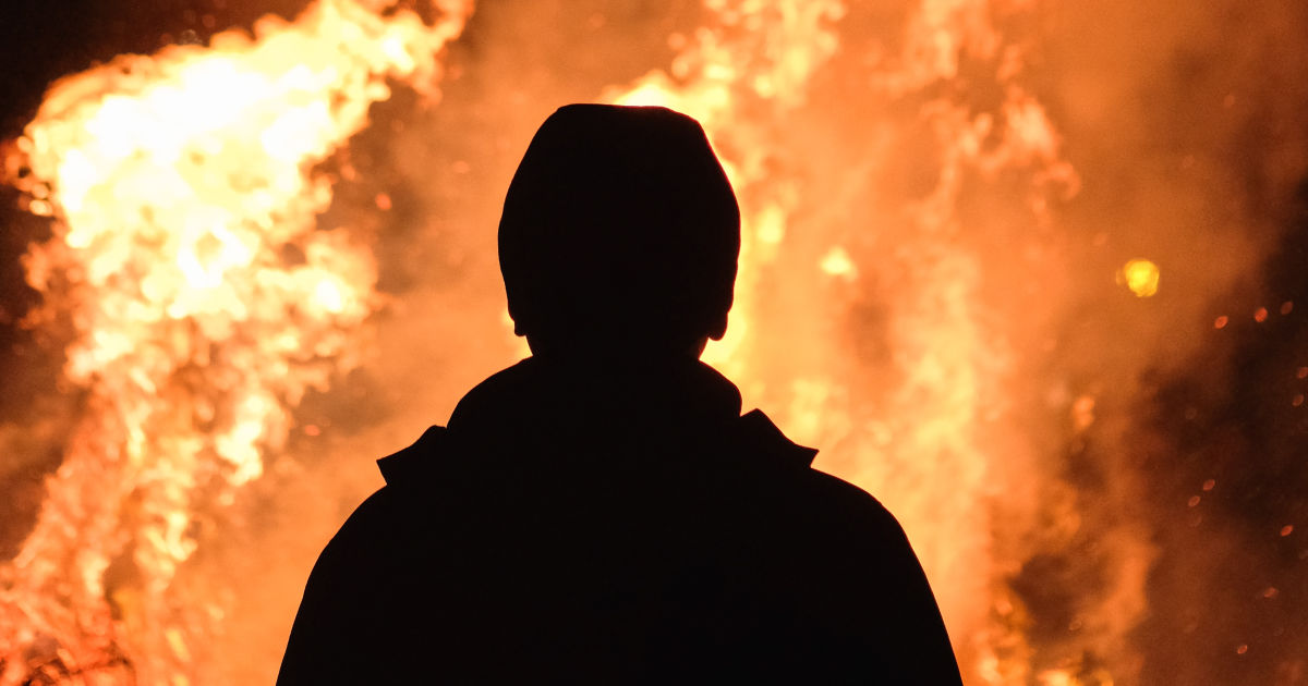 a dark silhouette of the back of a person watching a blazing fire