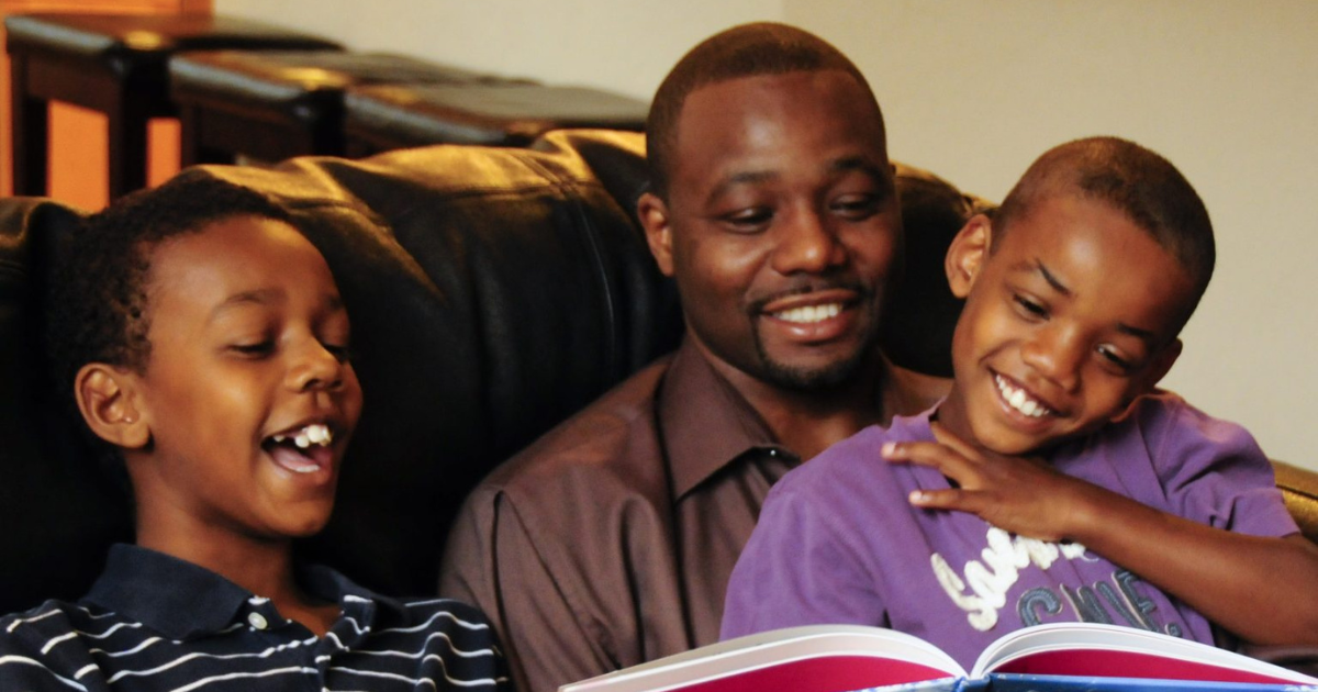 A dad reads a book to his two boys sitting on a couch